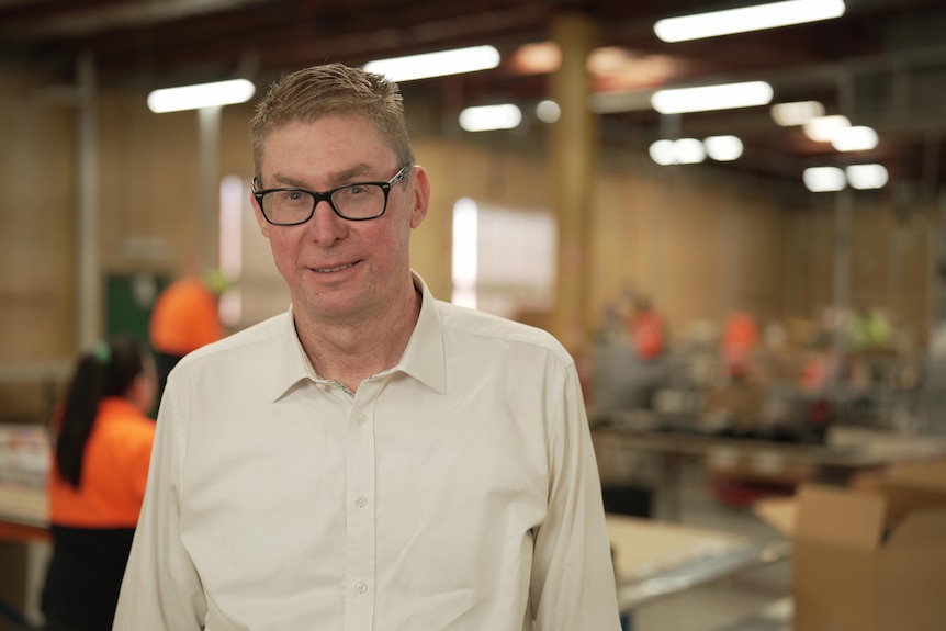 Middle-aged white man wearing a white shirt and glasses standing in a factory