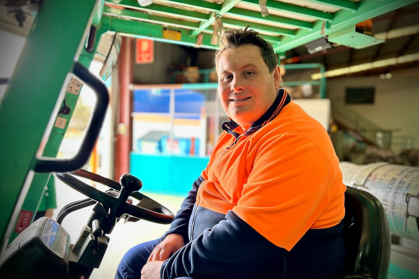 Caucasian man sitting on a forklift wearing orange high-vis equipment