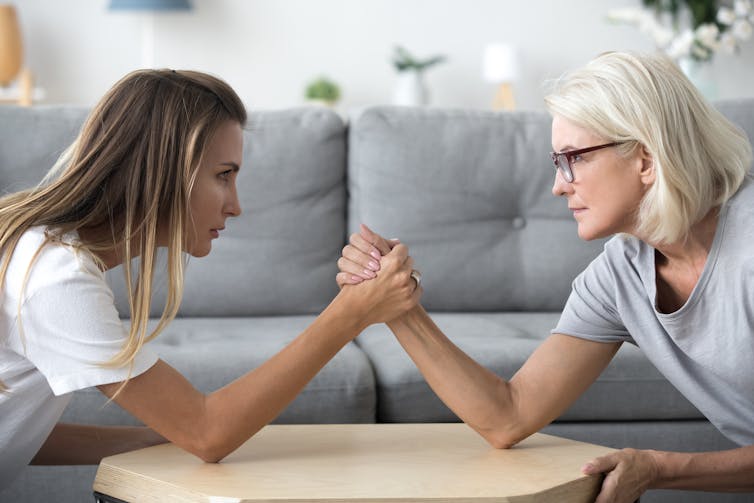 Two women from different generations arm wrestle.